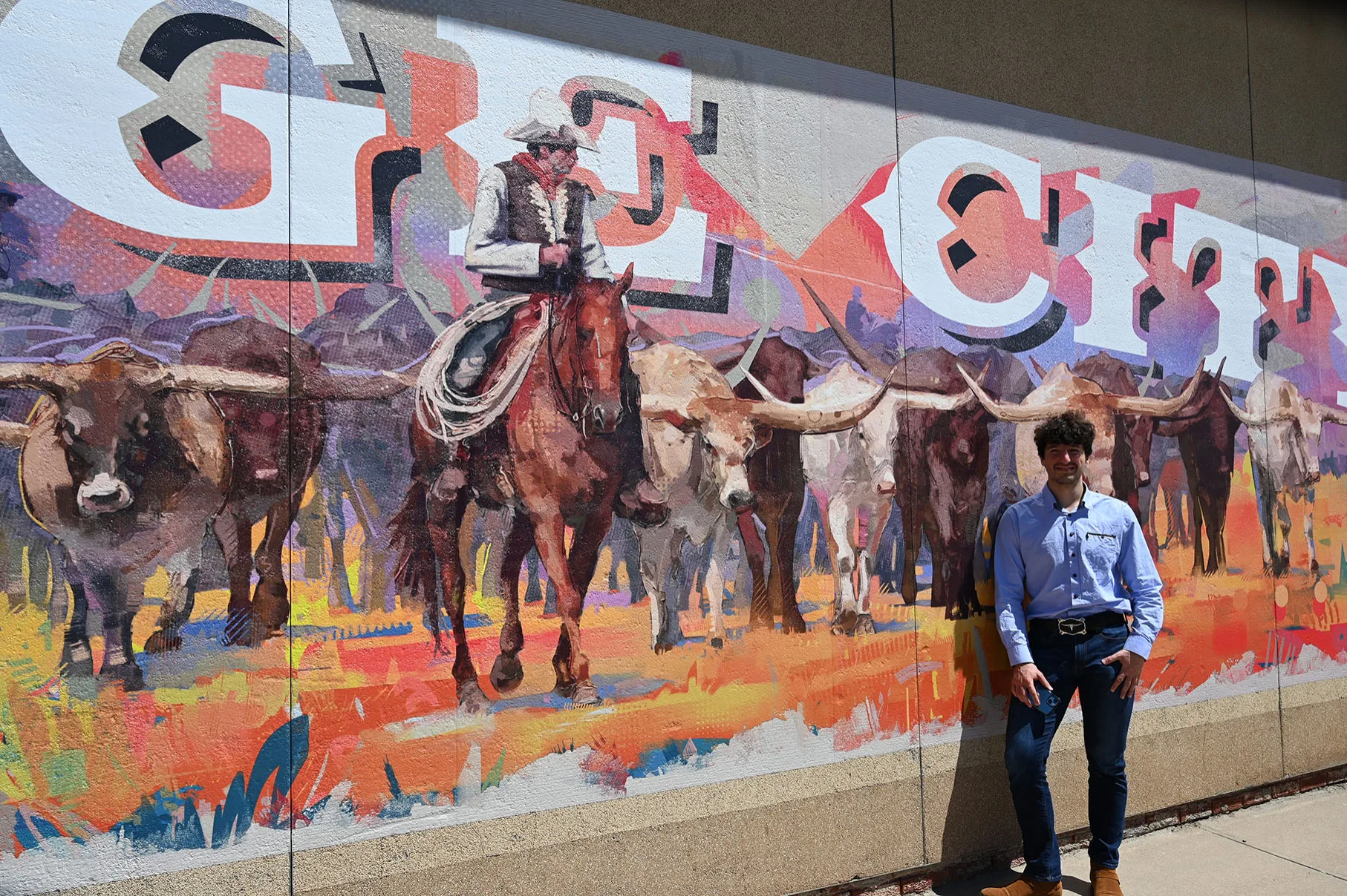 The installed cattle drive mural with a person standing against it, showing the longhorns at roughly life size