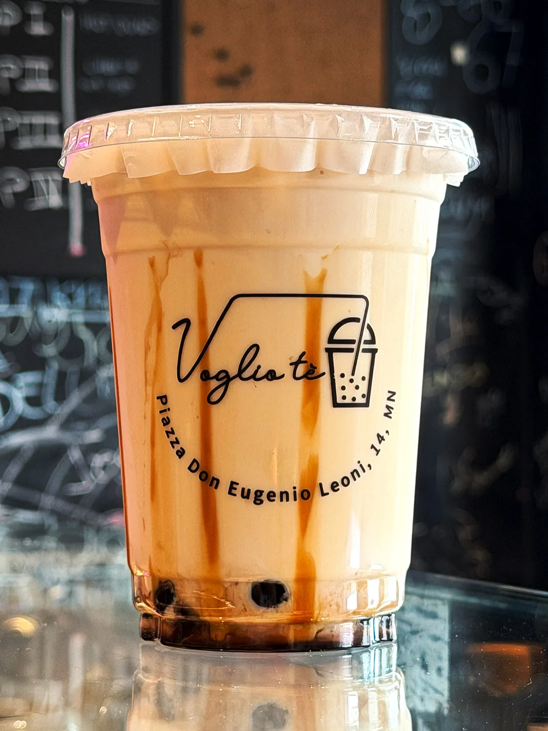 Brown sugar fresh milk latte with tapioca pearls and syrup streaks, on the counter in front of the chalkboard menu