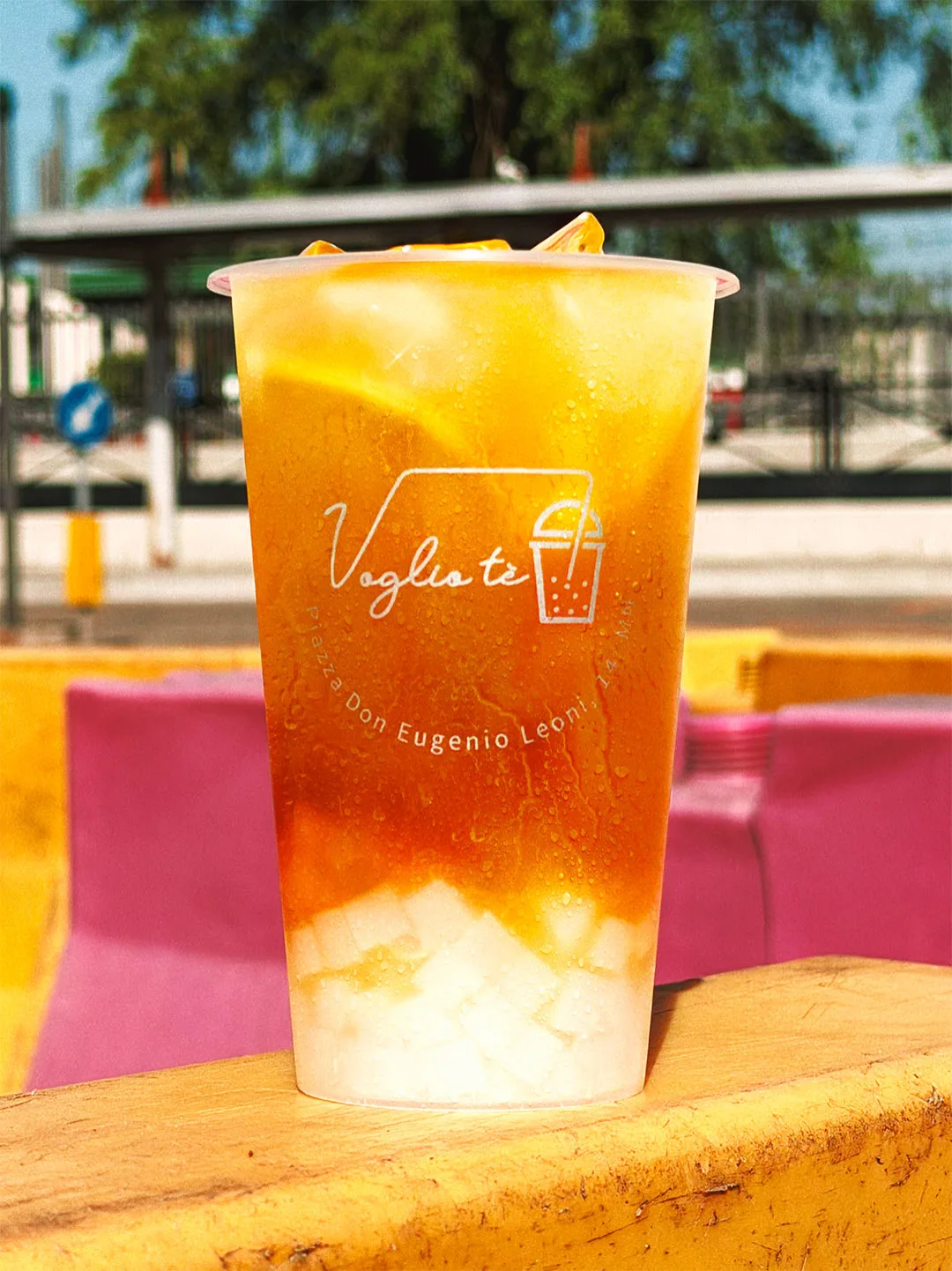 Passion fruit and mango fruit tea with coconut jelly, standing on a yellow road barrier in the sun
