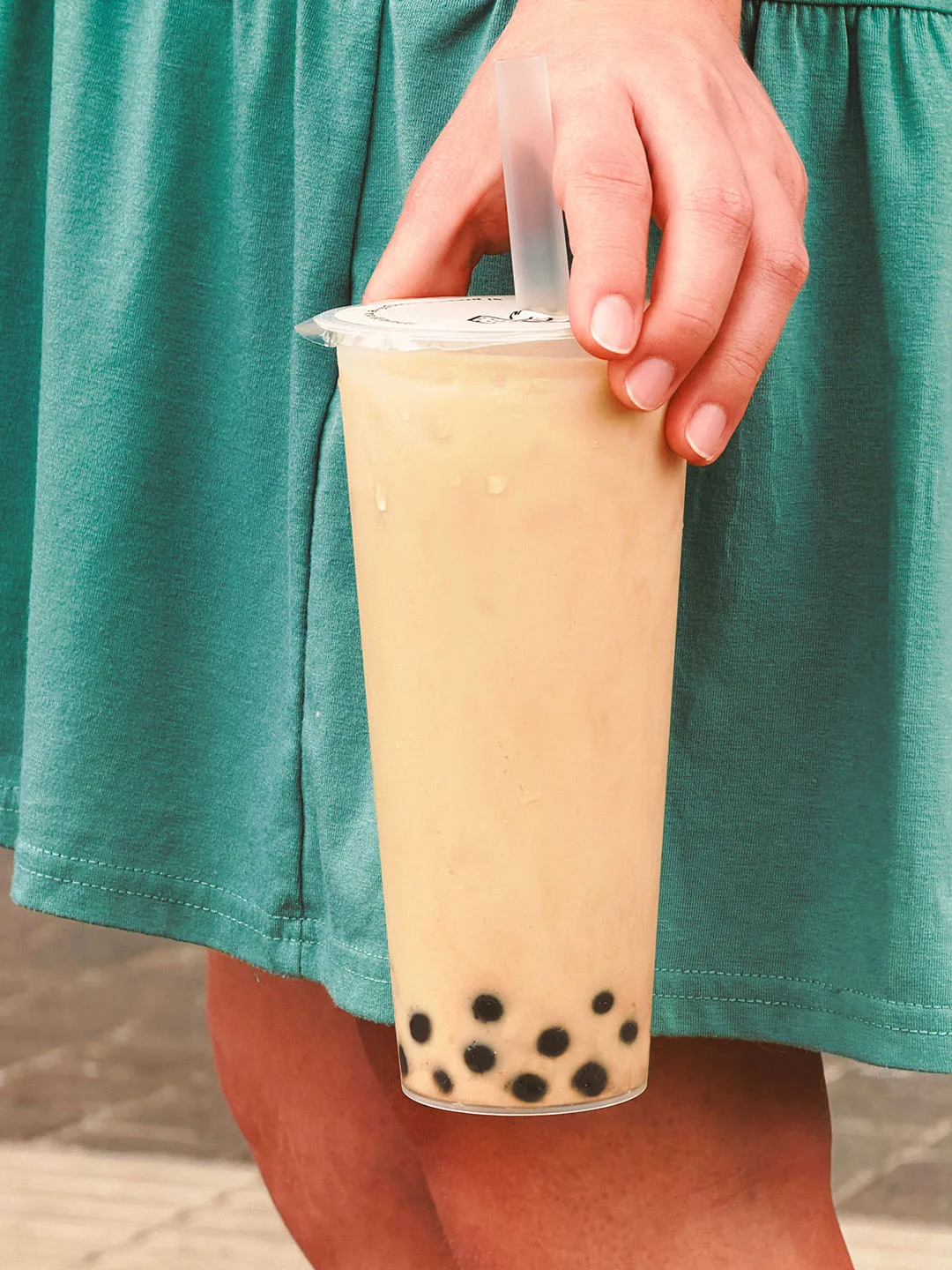 Classic milk tea with tapioca pearls, carried at the hip against a green dress on a cobbled street