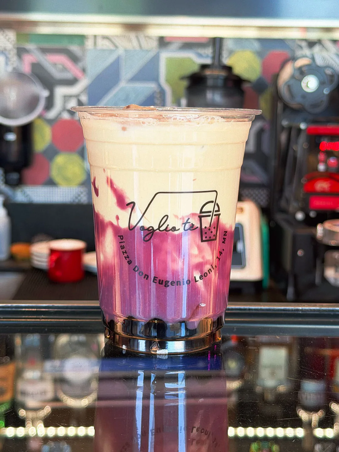 Taro milk tea, cream over purple, on the counter with the espresso machine behind it